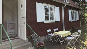 A house with a red exterior, white shutters, and a small porch with a table and chairs. - Beachfront classic summer cottage for the family in Ahus. Ideal for families with children (Åhus)