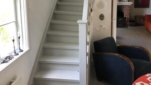A staircase with white walls and a radiator, leading to a room with a fireplace and a red chair. - Beachfront classic summer cottage for the family in Ahus. Ideal for families with children (Åhus)