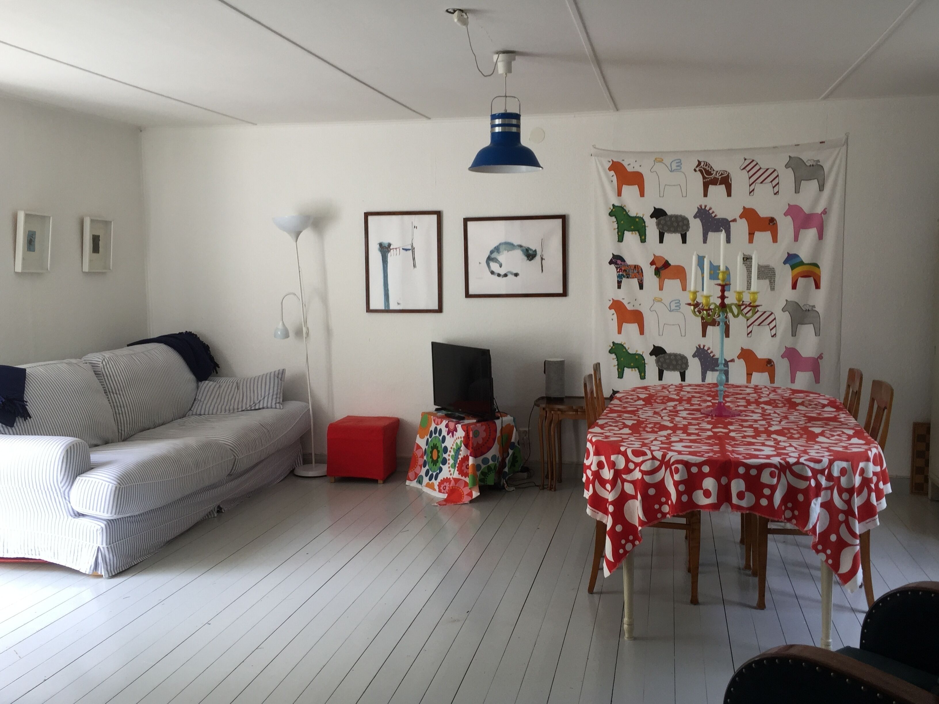 A living room with a striped sofa, a red ottoman, a TV, a table with a red tablecloth, and a wall with animal prints.