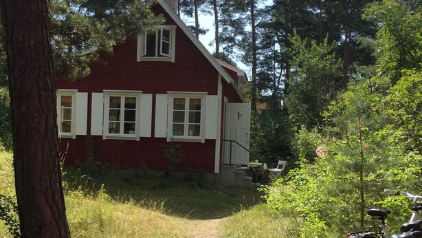 A red house with white trim, surrounded by trees and a gravel path. - Beachfront classic summer cottage for the family in Ahus. Ideal for families with children (Åhus)
