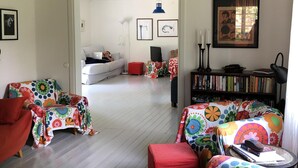 A living room with colorful floral upholstery, a red armchair, a bookshelf, and a view into another room. - Beachfront classic summer cottage for the family in Ahus. Ideal for families with children (Åhus)