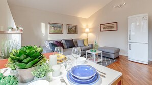 Un salon moderne avec un canapé, une table à manger dressée pour deux personnes et un réfrigérateur.