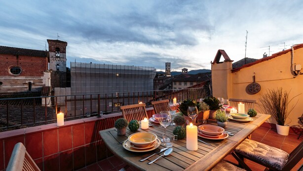 Une terrasse sur le toit, avec une table dressée pour le dîner, offrant une vue sur le paysage urbain et ses bâtiments historiques.
