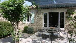 Ein Steinhaus mit einer Terrasse, die Gartenmöbel und eine Pergola hat.