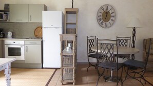 Eine kleine Küche mit einem weißen Kühlschrank, einer Mikrowelle und einem Herd. Es gibt einen Esstisch mit Stühlen und eine an der Wand befestigte Uhr.
