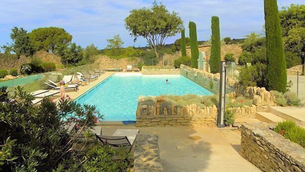 Ein Poolbereich mit Steinmauern, wenigen Liegestühlen und blauem Himmel.