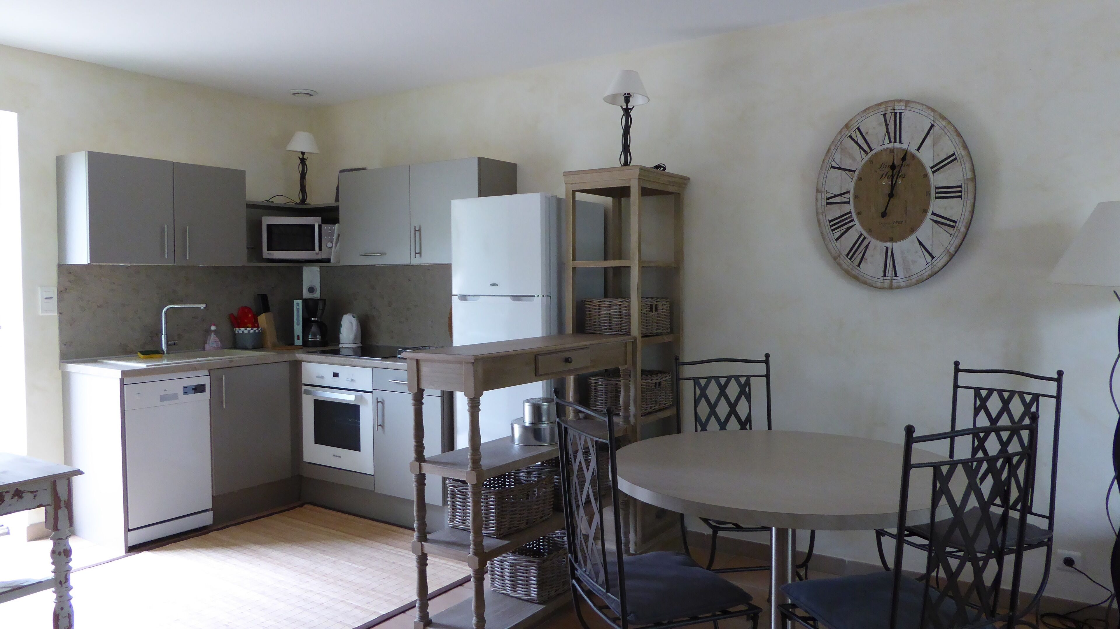 A compact kitchen with a dining area, including a clock and wicker baskets.