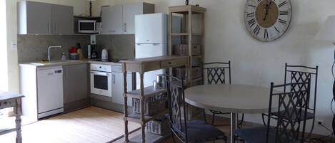 A compact kitchen with a dining area, including a clock and wicker baskets.