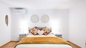A bedroom with a bed, two nightstands, an air conditioner, and decorative plates on the wall.
