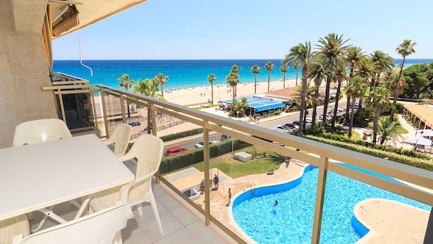 A balcony with a view of a beach, pool, and palm trees.