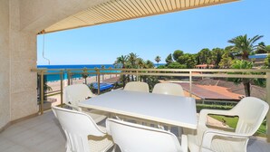 A balcony with a table and chairs, overlooking a beach and palm trees.