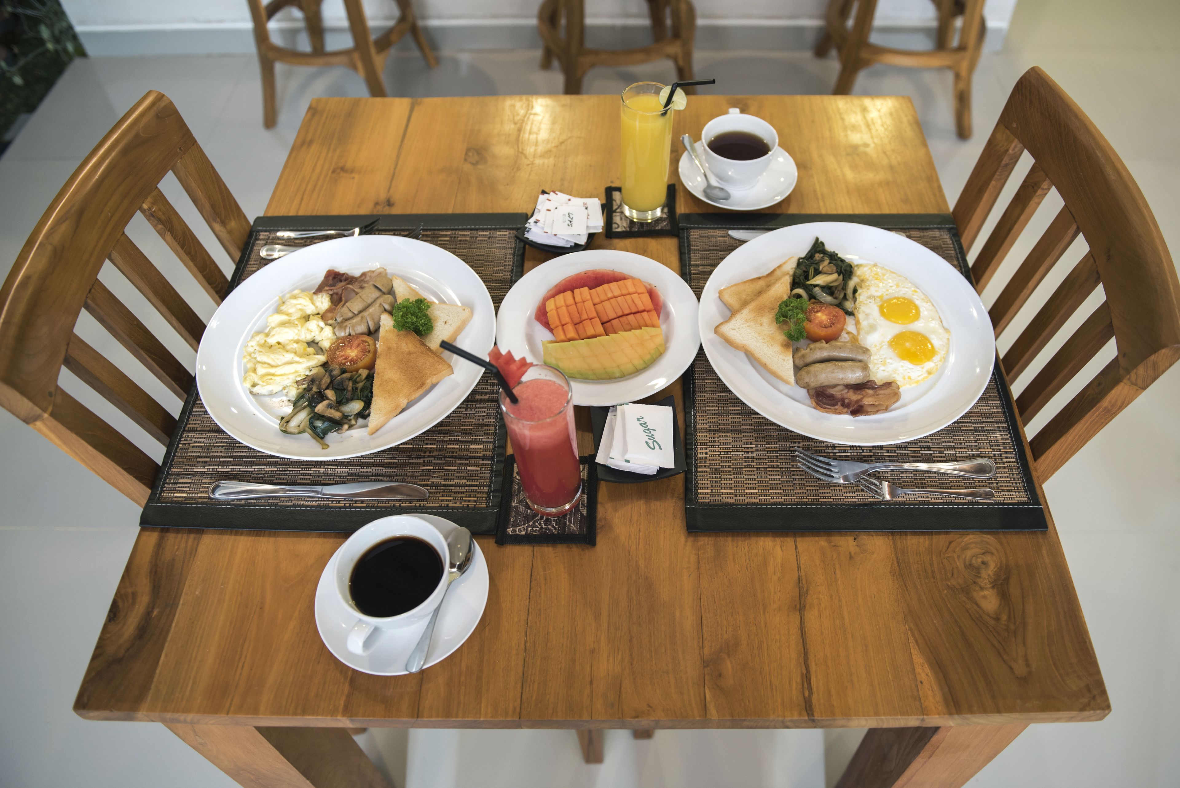 Une table de salle à manger en bois, avec quatre assiettes remplies de nourriture, deux tasses de café et un verre de jus d’orange.