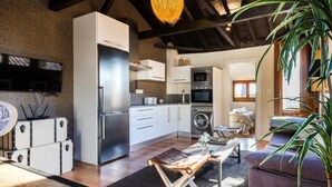 A modern kitchen with a built-in oven and microwave, a dining area with a wooden table and bench, and a living room with a sofa and a large plant. - Fantastic penthouse with terrace and views (Granada)