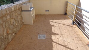 Een balkon met stenen vloer, een metalen hekwerk en een klein ventilatierooster.