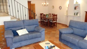 Een woonkamer met twee blauwe banken, een eettafel met stoelen, een trap en een kroonluchter.