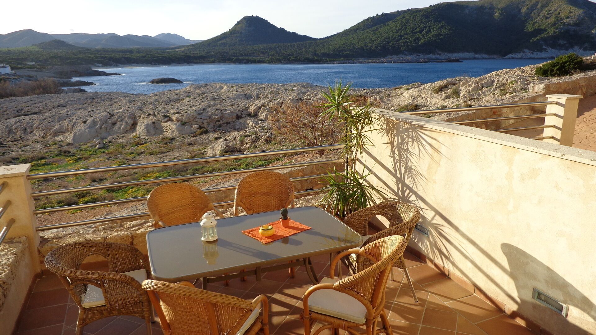 Une terrasse dotée de chaises et d’une table en osier, offrant une vue sur une côte rocheuse et une étendue d’eau.