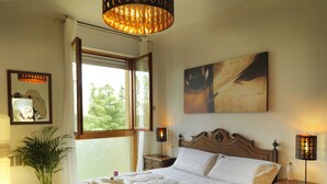 A neatly made bed with a headboard, bedside tables with lamps, a large window with curtains, and a painting on the wall. - Bellaria Park "Hills View" Residences (san lazzaro di savena (Bologna))