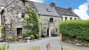 Un bâtiment en pierre, orné de lierre, avec des plantes en pot et une allée gravillonnée.