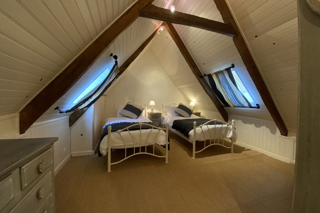 A bedroom with two beds, wooden beams, a dresser, and a window.