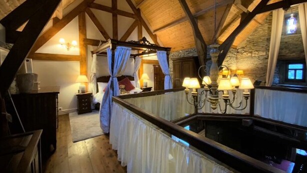 Une chambre avec un lit à baldaquin, des poutres en bois, des murs en pierre et une vue sur la pièce.