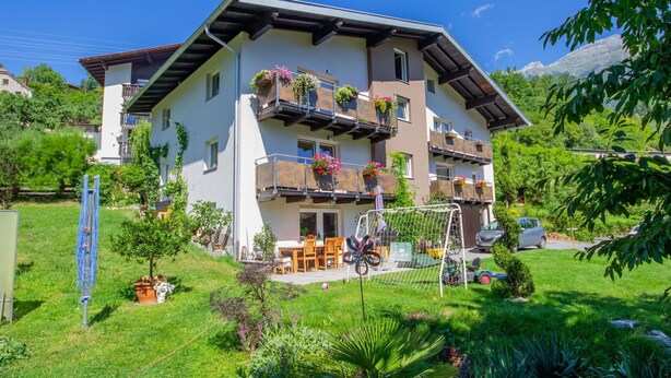 A multi-story building with balconies, a garden, and a mountain in the background. - Nice apartment for 4 guests with WIFI, TV and balcony (Pians)