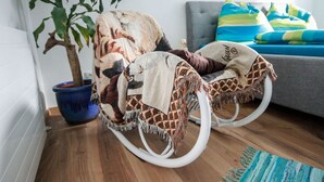 A rocking chair with a patterned blanket, a potted plant, and a grey sofa with colorful pillows in a living room with wooden flooring. - Nice apartment for 4 guests with WIFI, TV and balcony (Pians)