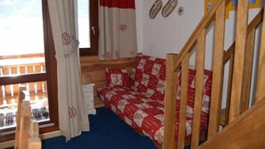 A cozy room with a wooden bed, a window with curtains, a wooden staircase, and a view of mountains. - Apartment in central Val Thorens on the slopes - magnificent view! (Les Belleville)