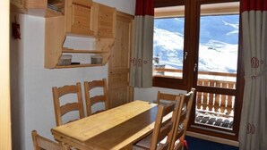 A wooden dining table with chairs, a wooden cabinet, and a window with a view of a snowy landscape. - Apartment in central Val Thorens on the slopes - magnificent view! (Les Belleville)