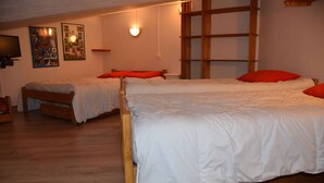 A room with two wooden beds, each with white bedding and red pillows. There is a wooden shelf unit against the wall and a wall-mounted television. - Apartment in central Val Thorens on the slopes - magnificent view! (Les Belleville)