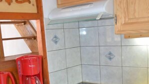 A compact kitchen with wooden cabinets, a white dishwasher, a red coffee maker, and a black stove. - Apartment in central Val Thorens on the slopes - magnificent view! (Les Belleville)
