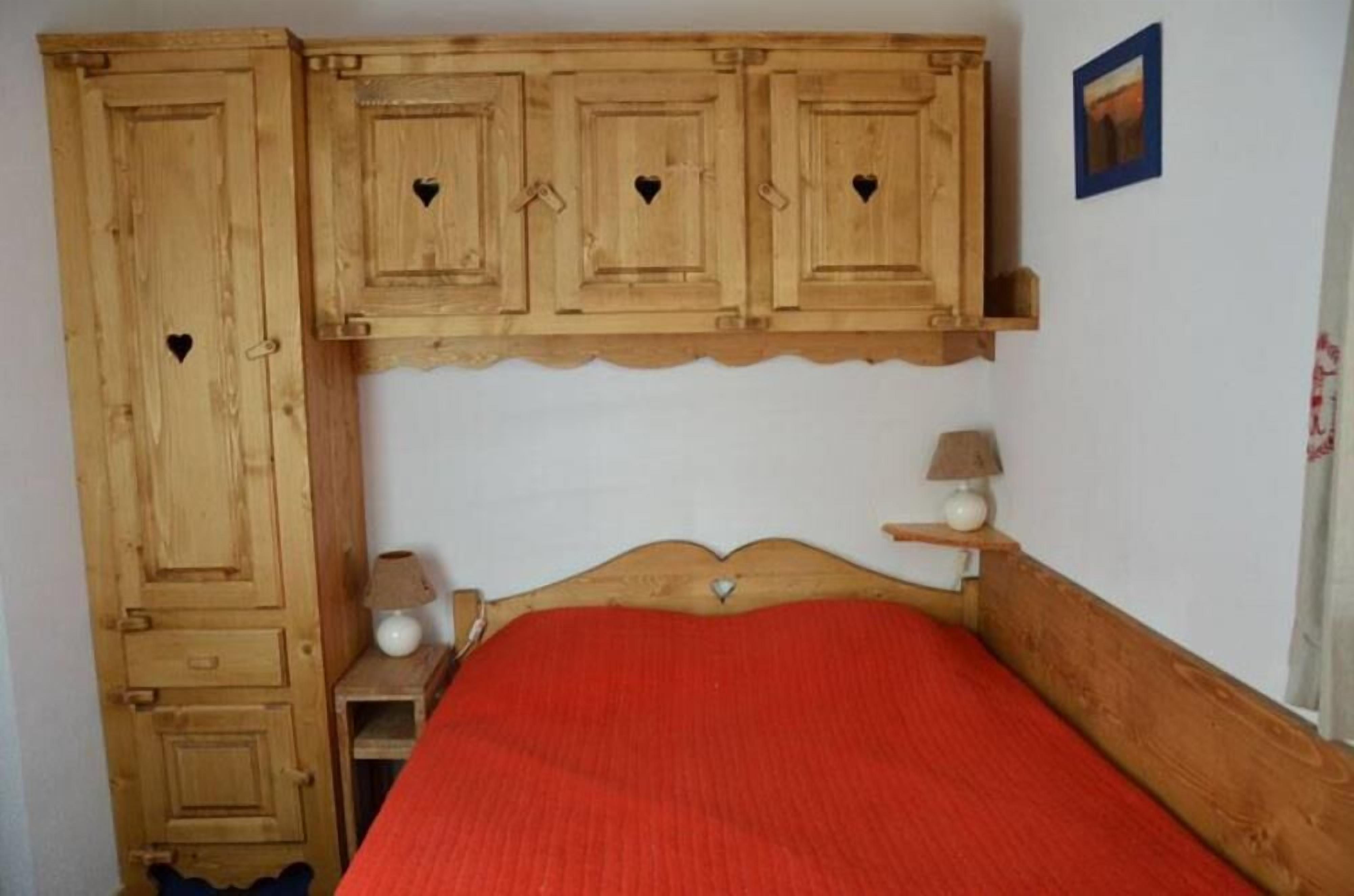 Une chambre à coucher avec un lit en bois, une couvre-lit rouge et une table de chevet sur laquelle sont posées deux lampes.