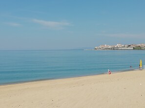 A beach with a clear sky, calm sea, and a distant town.