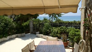 An outdoor patio with a table and chairs, a covered area, and a view of the sea.