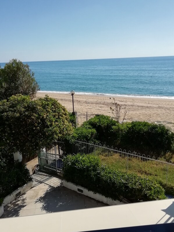 A beach view with a clear sky, a sandy shore, and a metal fence.