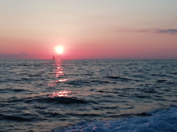 Atardecer sobre el océano con un barco a lo lejos.