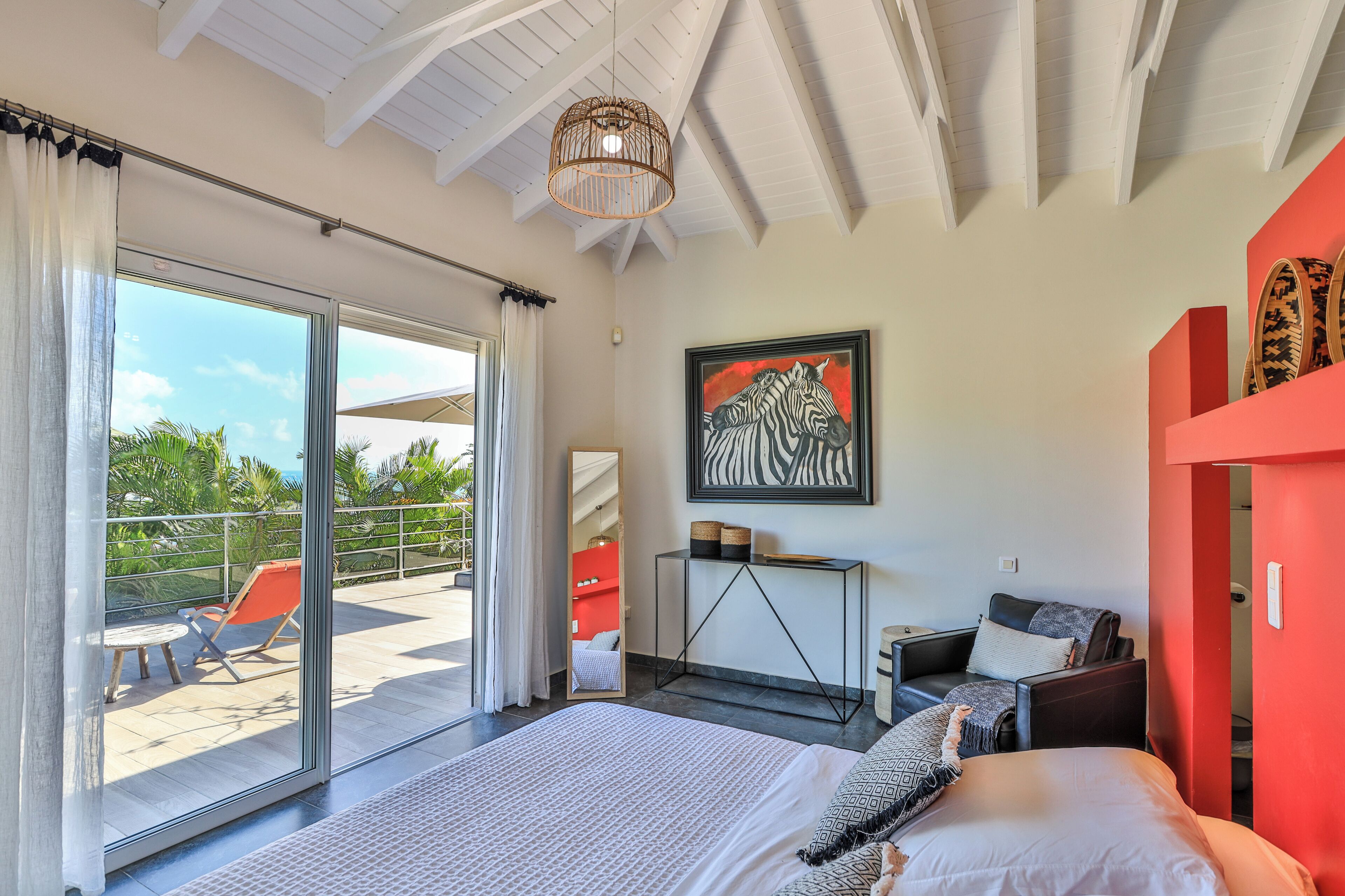 A bedroom with a large bed, a desk, a chair, and a balcony with a view of the outdoors.
