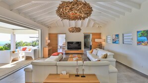 Ein geräumiges Wohnzimmer mit einem großen weißen Sofa, einem Holztisch und einem auffälligen Holz-Chandelier.