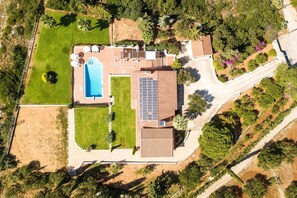 Vista aérea de una propiedad con piscina, paneles solares y un amplio jardín.