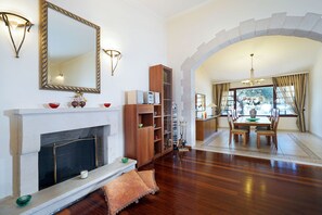 Una sala de estar con chimenea, estanterías de madera, un comedor con mesa y sillas, y un espejo grande en la pared.