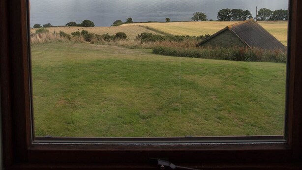 A view through a window of a grassy field, a body of water, and distant hills. - Uninterrupted sea views across the Moray Firth home to dolphins (Rosemarkie)