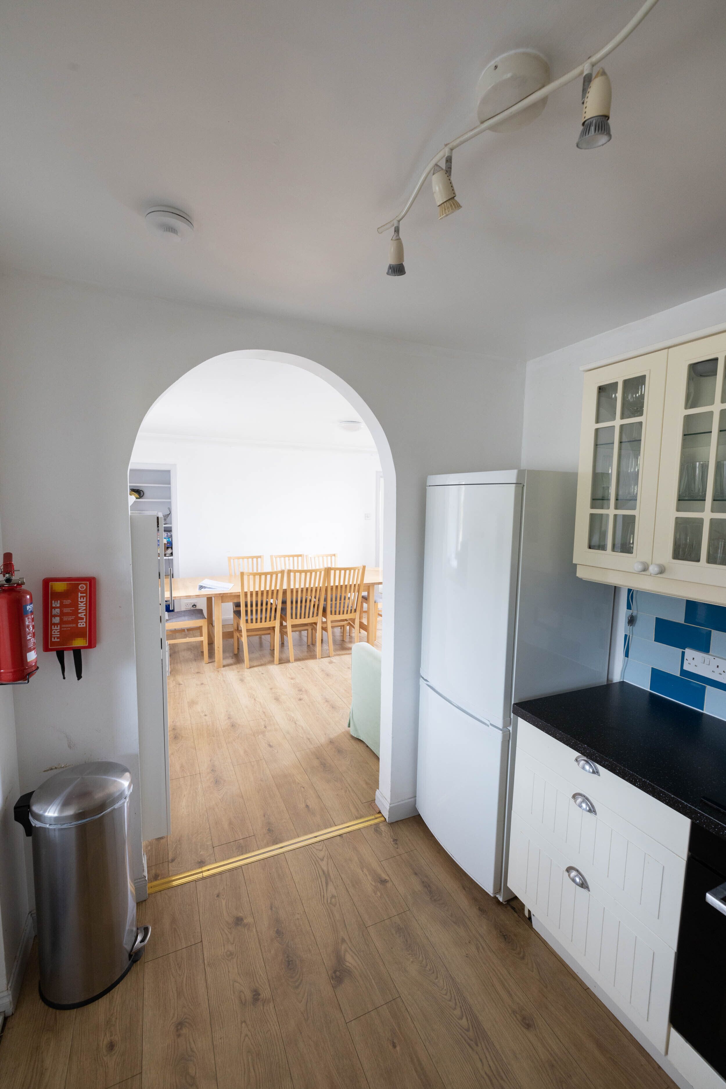 Een keuken met witte kastjes, een zwart aanrecht en een houten eettafel met stoelen.