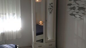 A bedroom with a white wardrobe, a bed with a blue bedspread, a bedside lamp, and a wall decoration of fish.