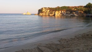 A beach with clear water, a sandy shore, and a rocky cliff with vegetation.