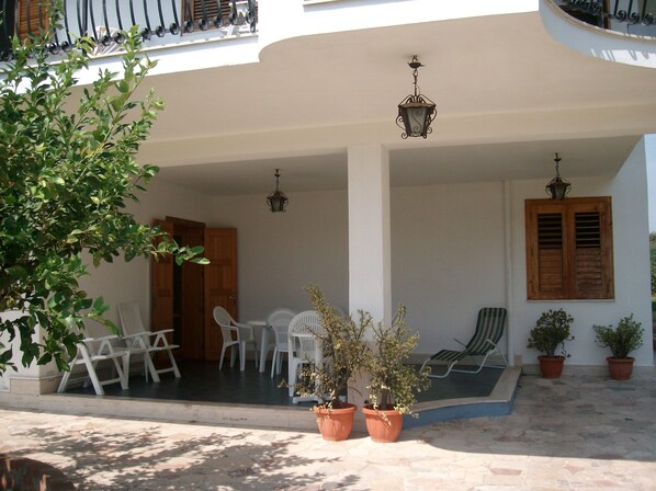A covered outdoor seating area with white plastic chairs, potted plants, and hanging lanterns.