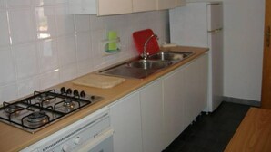 Une petite cuisine avec des meubles blancs, une cuisinière à gaz, un évier et un réfrigérateur.
