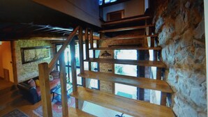 Eine mehrstöckige Holztreppe in einem rustikalen Innenraum mit Steinwänden und großen Fenstern.
