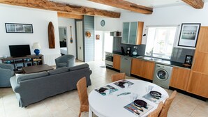 Un salon moderne avec un canapé gris, une table à manger avec des chaises et un coin cuisine doté de meubles en bois et d’un lave-linge.