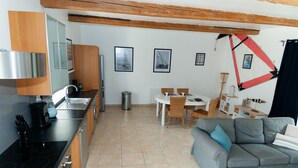 Une cuisine moderne équipée d’une cuisinière, d’un évier et de placards, un coin repas avec une table et des chaises, et un canapé gris agrémenté d’un coussin bleu.
