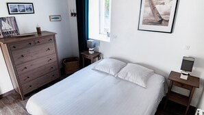 Une chambre bien rangée, avec un grand lit, une commode, une table de chevet et une fenêtre donnant sur la mer.