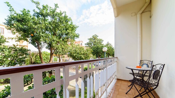 A balcony with a white railing, a small table with chairs, and a view of trees and buildings. - Casa Laura Orange (Sant´Agnello)